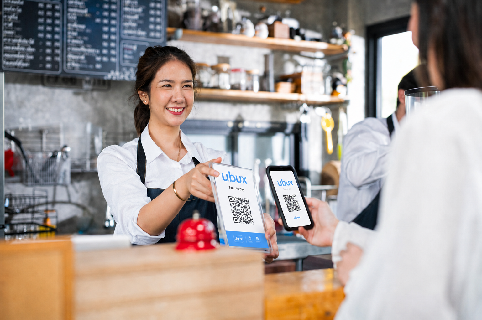 Cafe staff member showing a UBUX scan-to-pay QR code to a customer